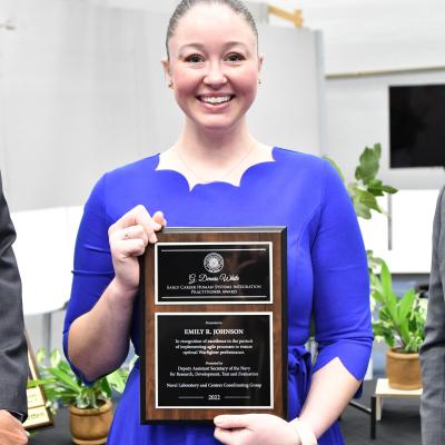 woman smiling in blue dress holding award plaque