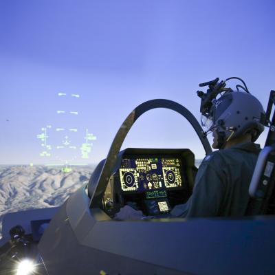 A pilot operates a fighter jet cockpit in a domed simulator.