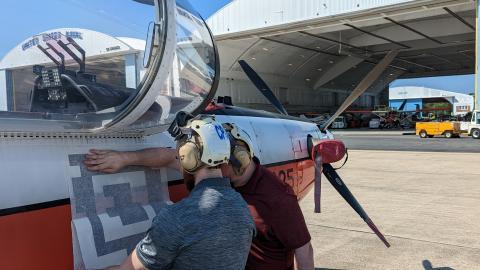 Engineers apply a fiducial tag along the side of a T-6 Texan aircraft in front of a hangar at the U.S. Naval Test Pilot School.
