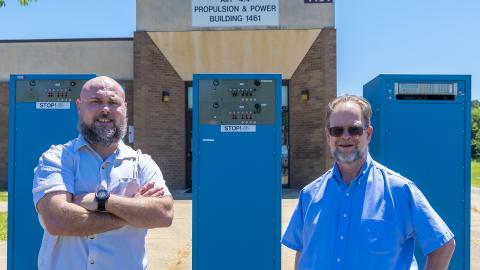 Senior Electrical Engineer Joshua Masters, left, and F-18 Electrical Subsystem Integrated Product Team  Lead Charles Singer stand in front of the computer-programmable power testing system they and other NAWCAD engineers invented to reduce the time required to test the avionics systems of the Navy's F/A-18 Hornets. The team, which received a patent for their invention, was recently recognized for their accomplishments in a virtual ceremony along with other patent awardees.