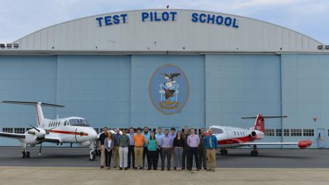 Civilian engineers from NAWCAD line up for a photo in front of U.S. Naval Test Pilot School's hangar in front of schoolhouse aircraft.