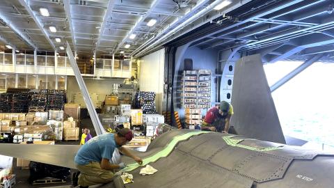 Two men repair F-35C Lightning II aircraft in hangar aboard aircraft carrier