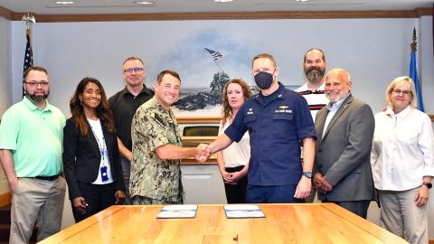 Group poses behind table as two commanders shake hands