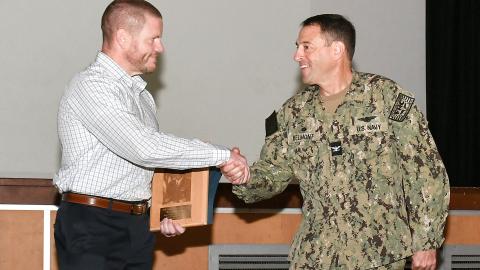 Navy captain shakes hand with civilian employee during award presentation
