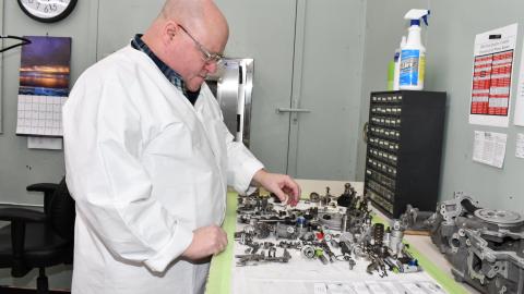 Aircraft maintainer in lab coat examines disassembled fuel control unit on clean room work bench