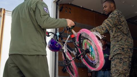 Man handing another man a children's bike with pink tires. 
