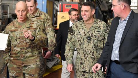Group of military officials walks down aisle in aircraft hangar