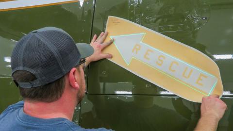 Man applying "rescue" arrow to side of green aircraft