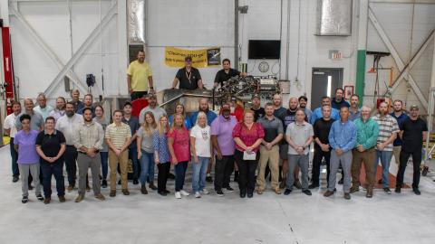 Group of people stand in front of aircraft engine 