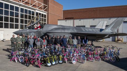 Group of people stand in front of aircraft with lots of children's bikes