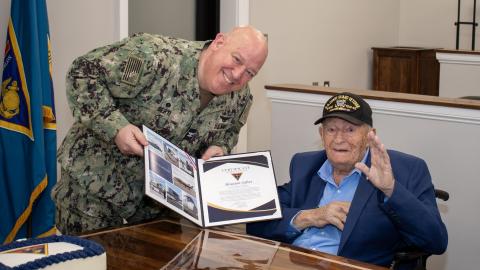 Man in military uniform holds up award with elderly man 