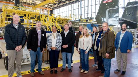 Group photo of people standing on red isle in an aircraft hangar