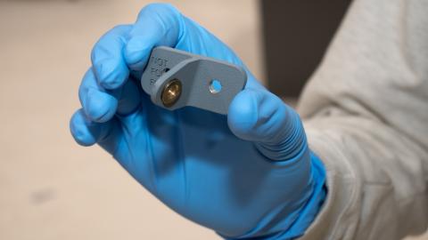 Person wearing blue gloves holds small grey metal part