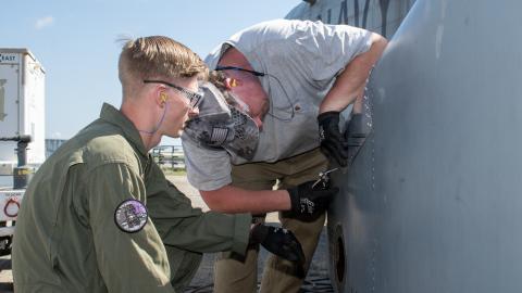 Marine and man in grey shirt work on exterior of military aircraft 