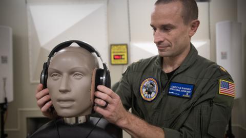 An aeromedical officer fits a dummy with headphones for audio testing in a lab.