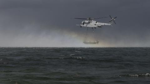 Helicopter hovering over open ocean carrying an inflatable boat