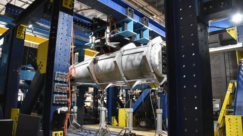 A metal fuel pod is mounted onto test equipment in a laboratory.