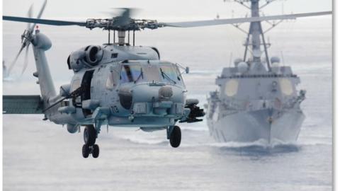 An MH-60 helicopter flying over a DDG in open ocean