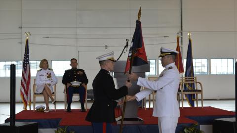 Lt. Col. Matthew Baumann takes a command flag from Cmdr. Daniel short in an aircraft hangar.