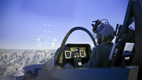 A pilot operates a fighter jet cockpit in a domed simulator.